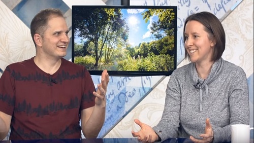 Curtis and Chelsea sit together at the anchor desk, in front of an image of beautiful green trees and blue skies.