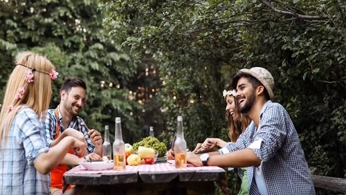 A group of four people eat a meal together outside at a picnic table. They look happy and are laughing.