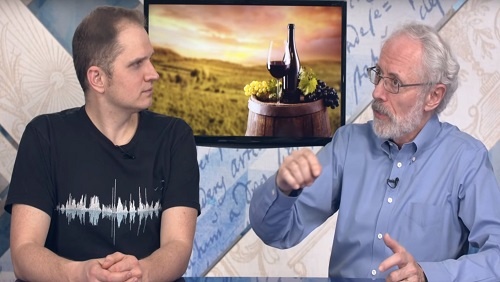 Curtis and Jonathan sit at the anchor desk, an image of a wine bottle, a wine glass, and grapes on a wine barrel behind them.