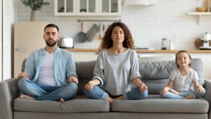 A man, woman, and child sitting on a couch in meditation poses.